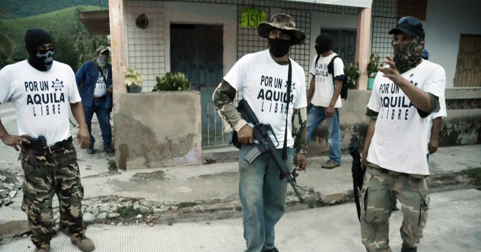 File-This July 23, 2013 file photo shows armed members of a local self-defense group wearing white T-shirts with the slogan For a Free Aquila stand at a street corner in the town of Aquila, Mexico. At least 23 bodies were found in two neighboring states in western Mexico where drug cartels, vigilantes and security forces have been fighting for much of the year, authorities said Saturday Aug. 17, 2013. The state prosecutor in Michoacan said that nine bodies, hands bound and shot, were found on an abandoned property near the town of Buenavista Tomatlan along with a sign indicating they may have been members of the Knights Templar cartel. (AP Photo/Gustavo Aguado, File)